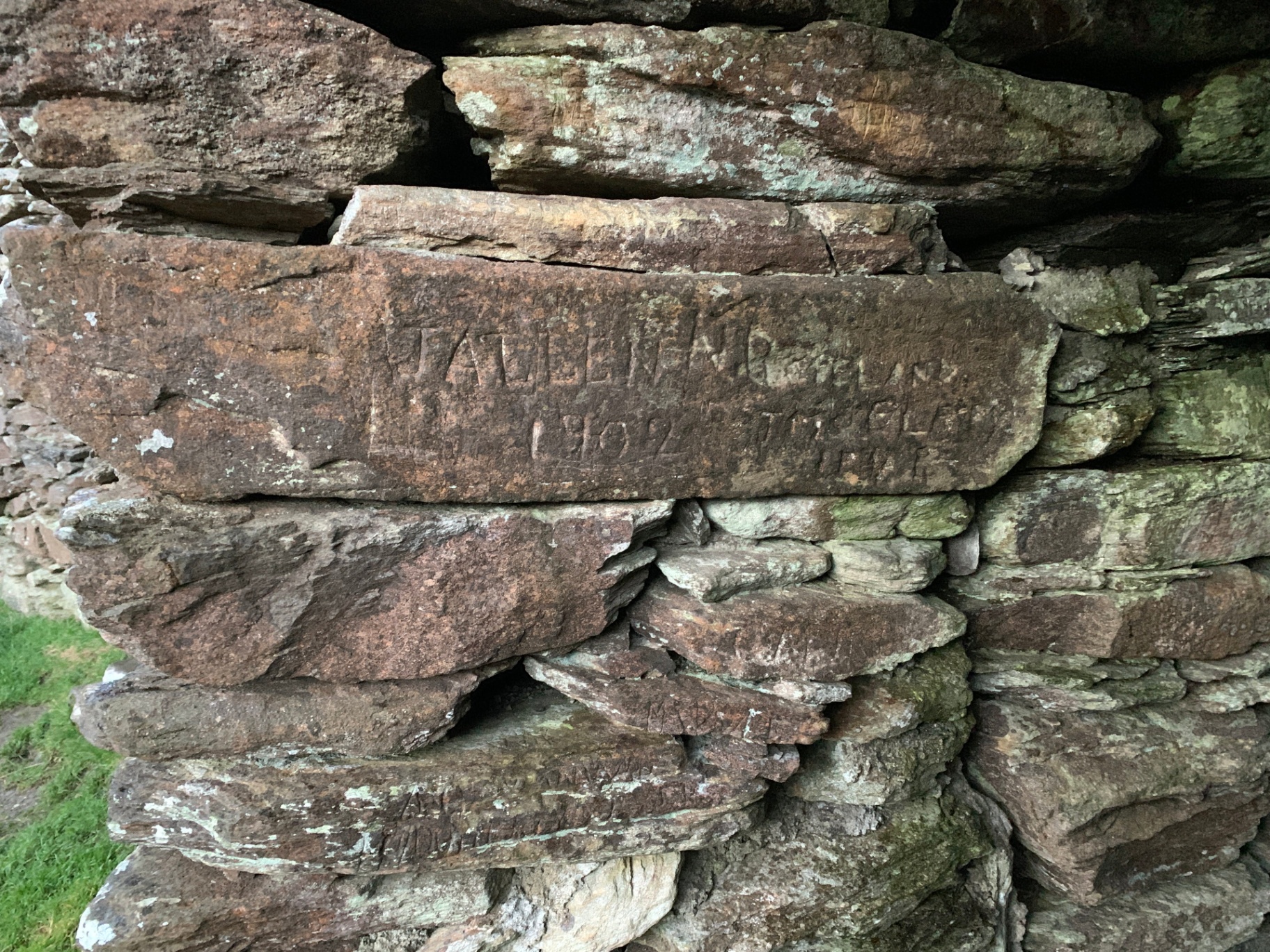 Historical visitor inscriptions including '1902' carved into the interior stones of Grianán of Aileach