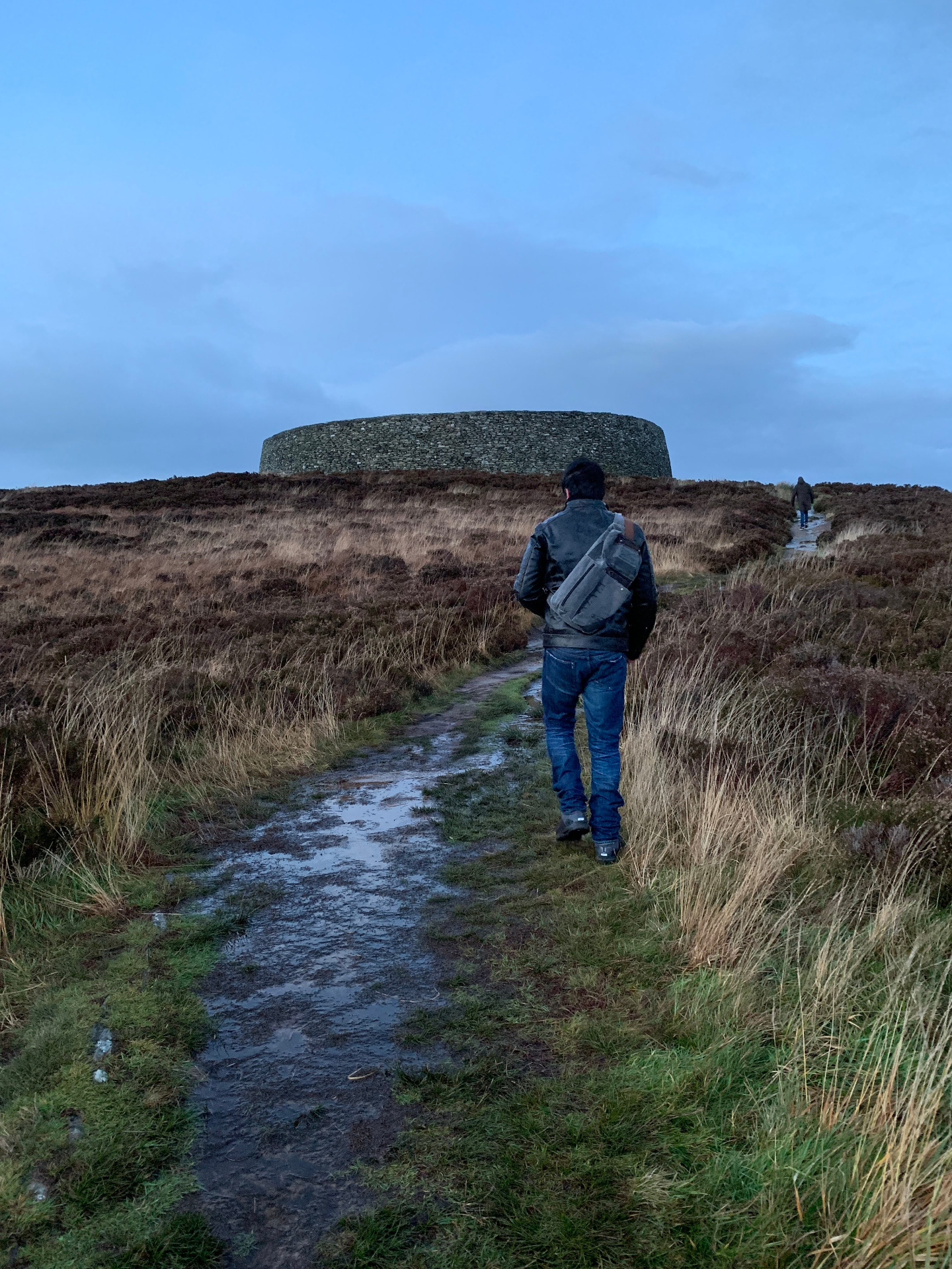 Visitor walking the muddy path up Greenan Mountain toward Grianán of Aileach at dusk