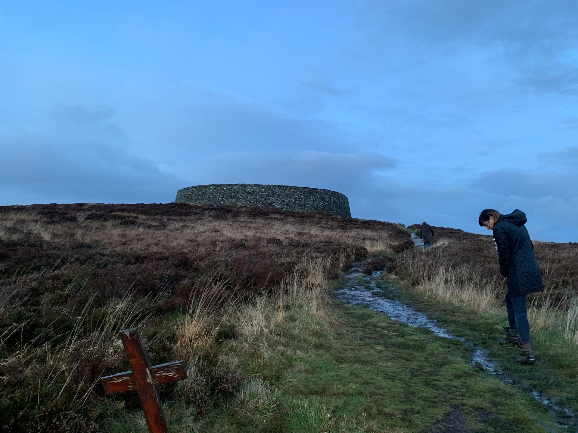 Wide view of Grianán of Aileach ringfort under blue evening sky with a wooden cross in the foreground